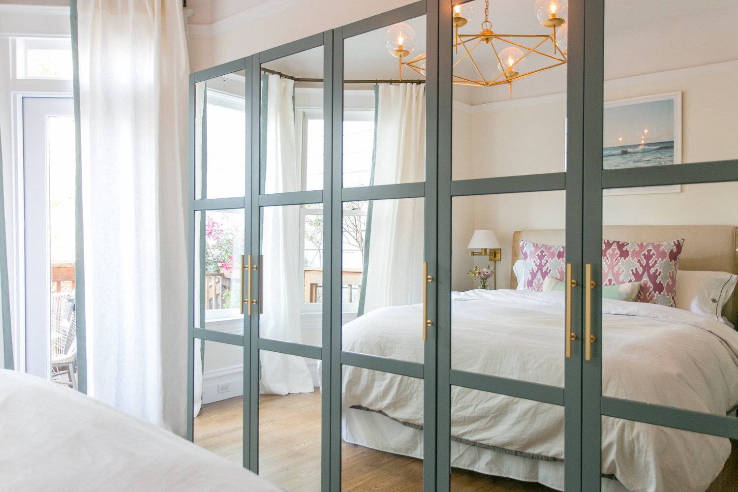 A bed with white bedding is reflected in a wall of mirrors.