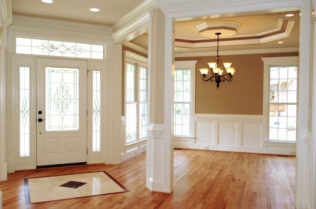 White living room with brown walls and wooden flooring, with white baseboard and crown molding wainscoting