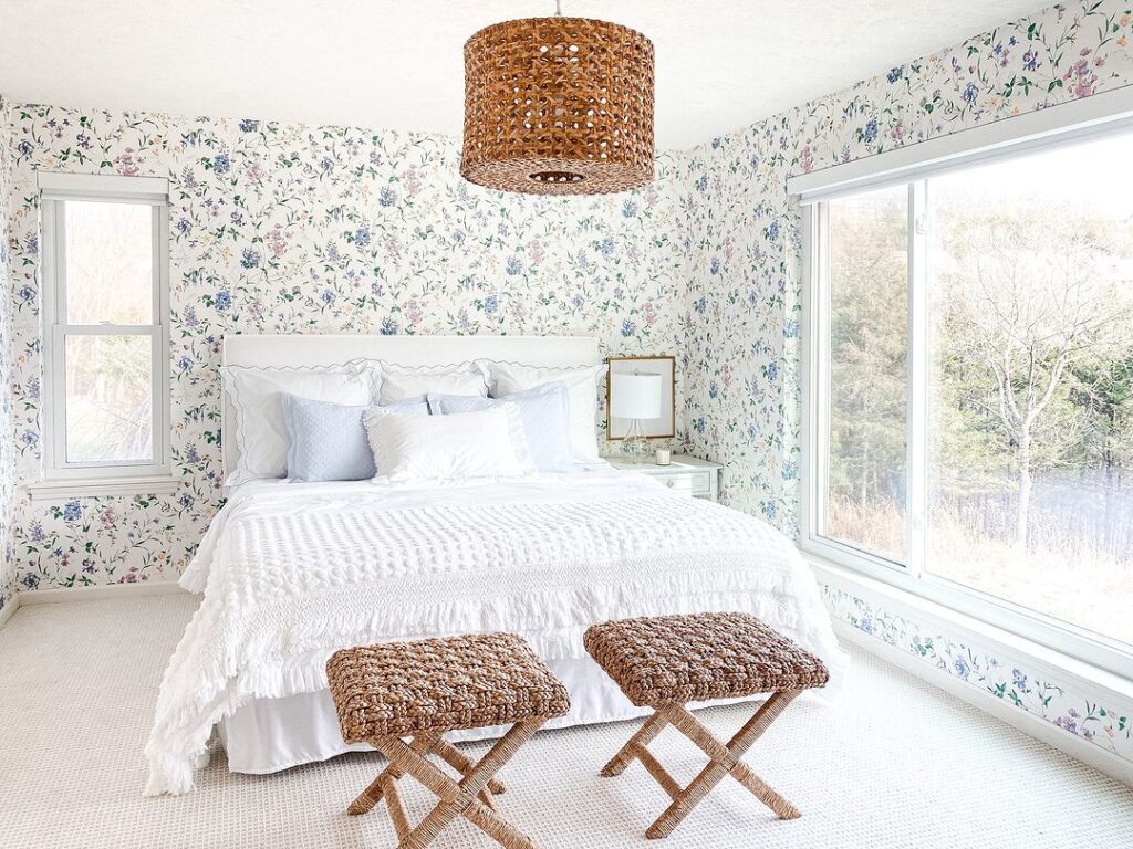 Light blue and brown floral wallpaper in bedroom with white large bed, large window and rattan hanging lamp.