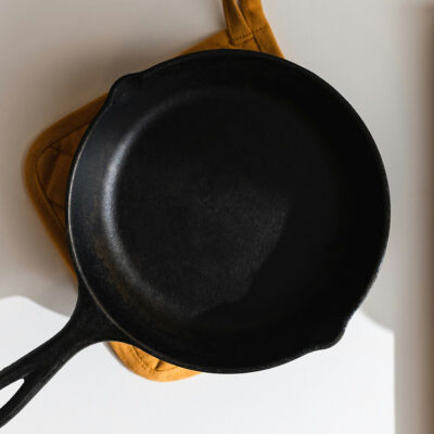 Close up of a cast iron pan and a yellow pot holder.