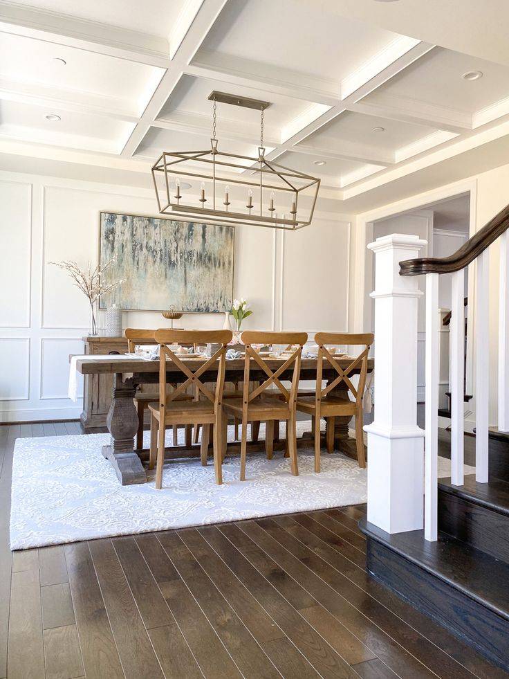 Large dining room with white rug and brown dining table in front of white wainscoting on wall